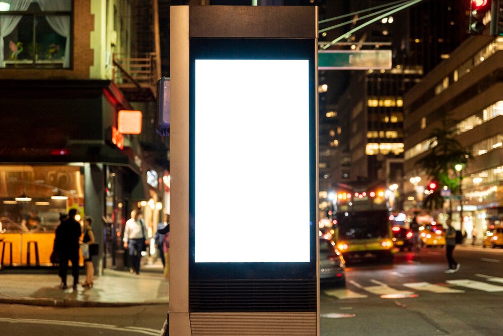 Foto de uma rua movimentada ao fundo, com um painel de led de mídia indoor em branco a frente, em destaque.