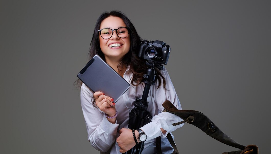 Foto de uma mulher sorrindo, de frente, segurando um tablet e uma câmera, pronta para criar um roteiro para vídeos.