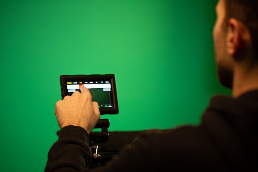 Operador ajustando a tela de uma câmera profissional em um estúdio com fundo verde (green screen), preparando-se para gravação com chroma key.