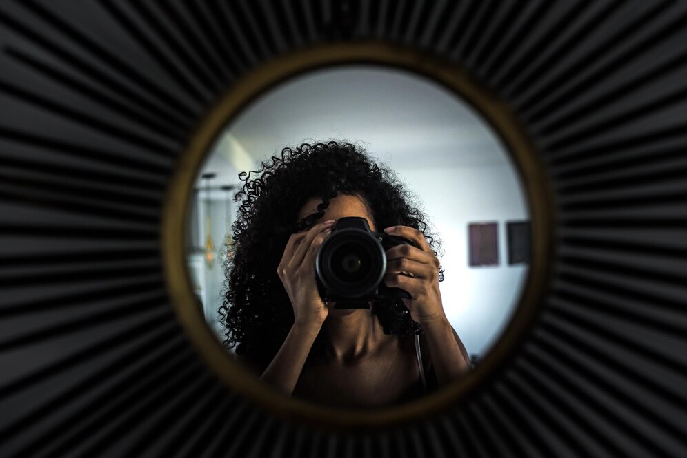 Fotografia de uma mulher tirando um autorretrato com uma câmera na frente de um espelho.